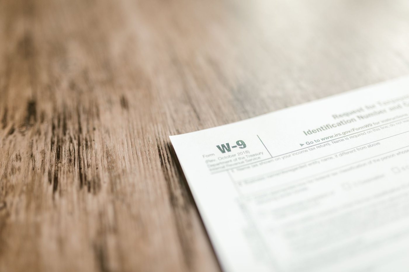 A blank IRS Form W-9, Request for Taxpayer Identification Number, lying at an angle on a weathered wooden table