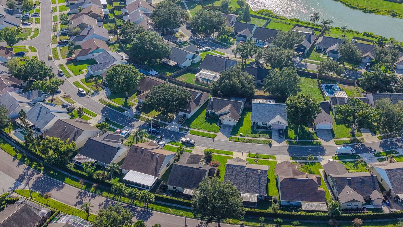 Aerial view of a Florida residential neighbourhood of low tile-roofed homes on curving streets, with screened pools and a lake at the top of the frame