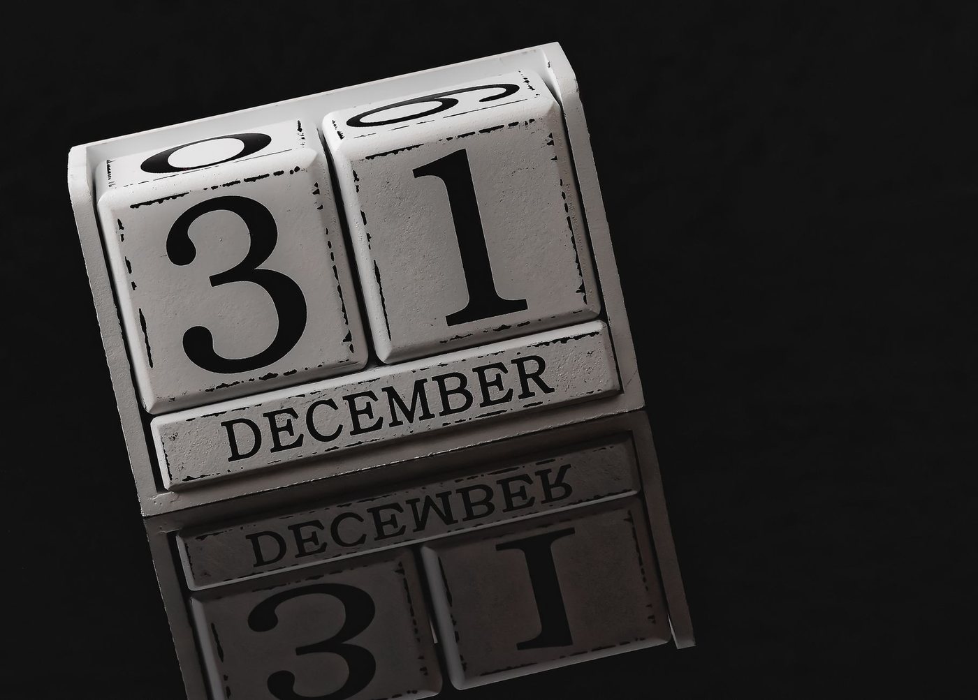 A wooden block calendar showing the date 31 December in black type on white blocks, reflected on a dark glossy surface