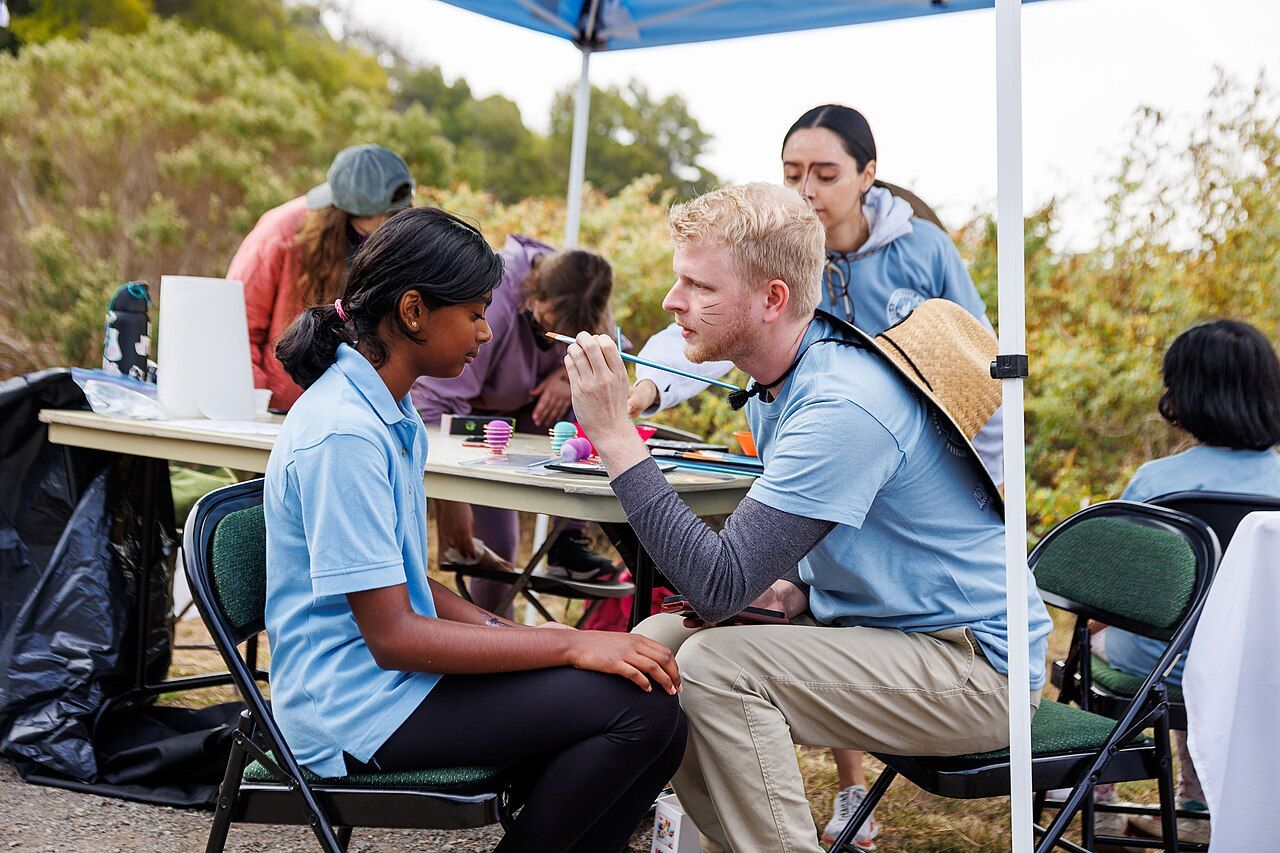 A volunteer face-paints a child at a community outreach event