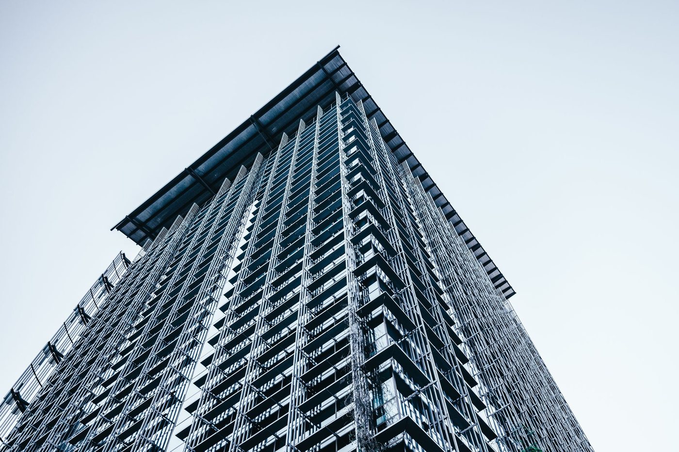 Low angle view of a tall modern office tower with a dense grid facade of glass and horizontal fins against a pale sky