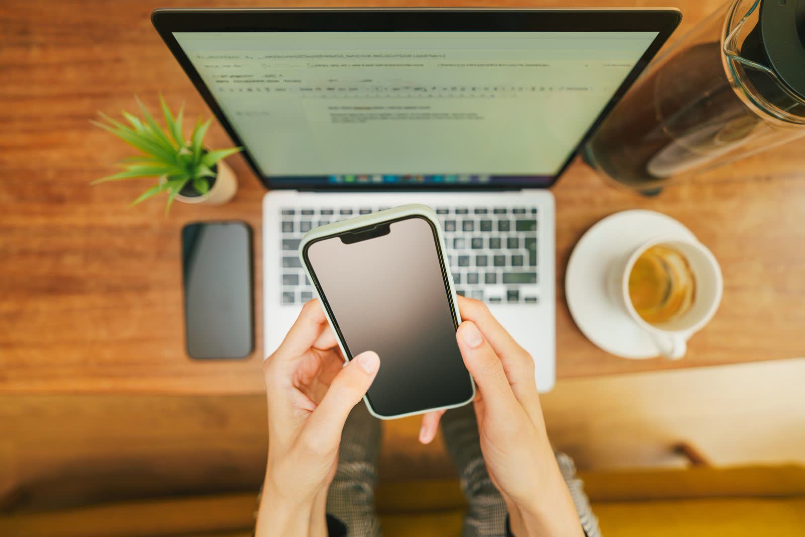 Hands holding a phone above a laptop and coffee