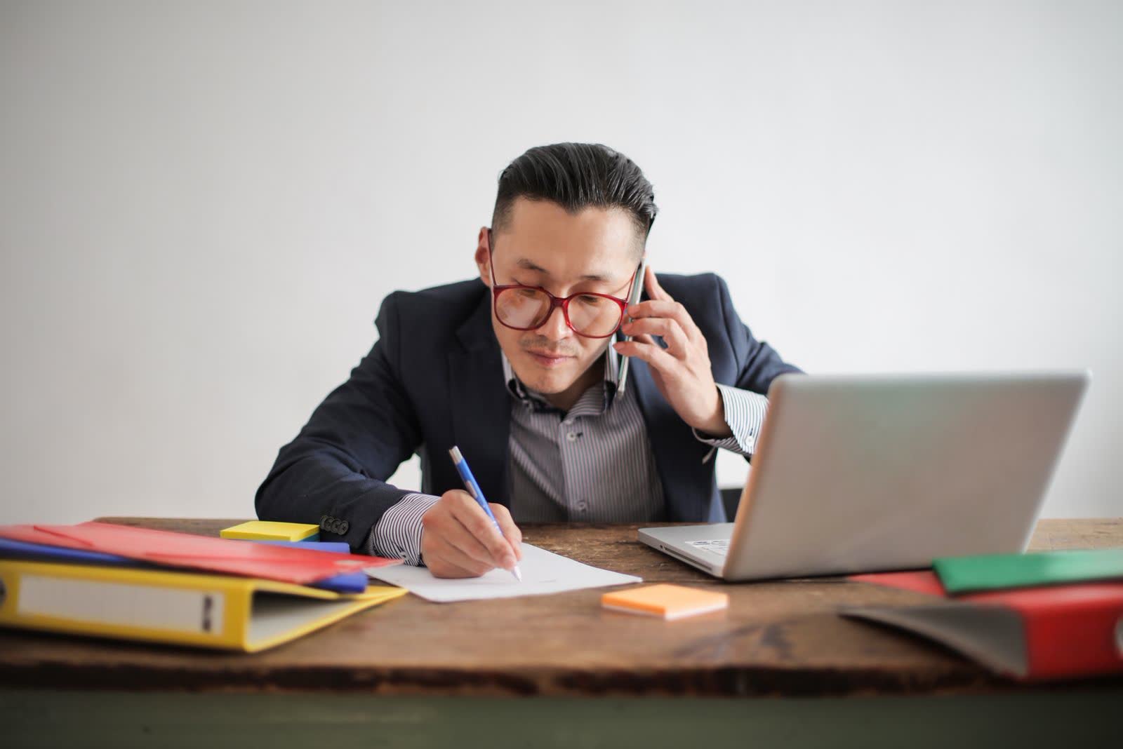 Businessman on a phone call taking notes beside his laptop