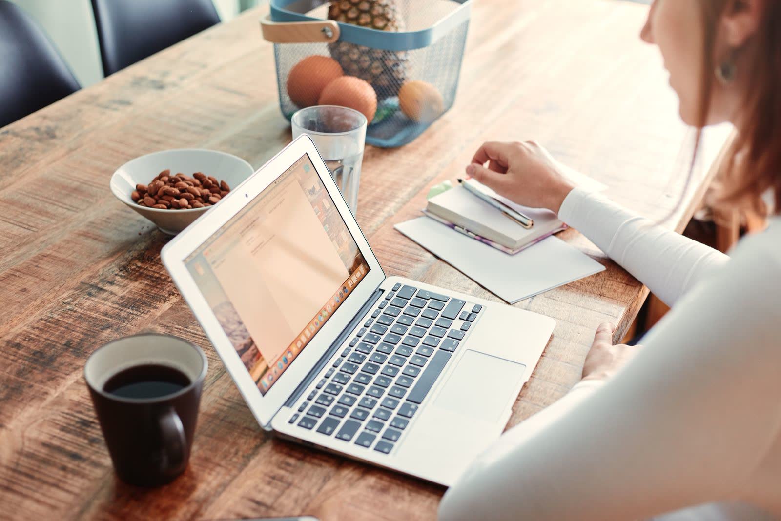 Writing in a notebook next to an open laptop and coffee