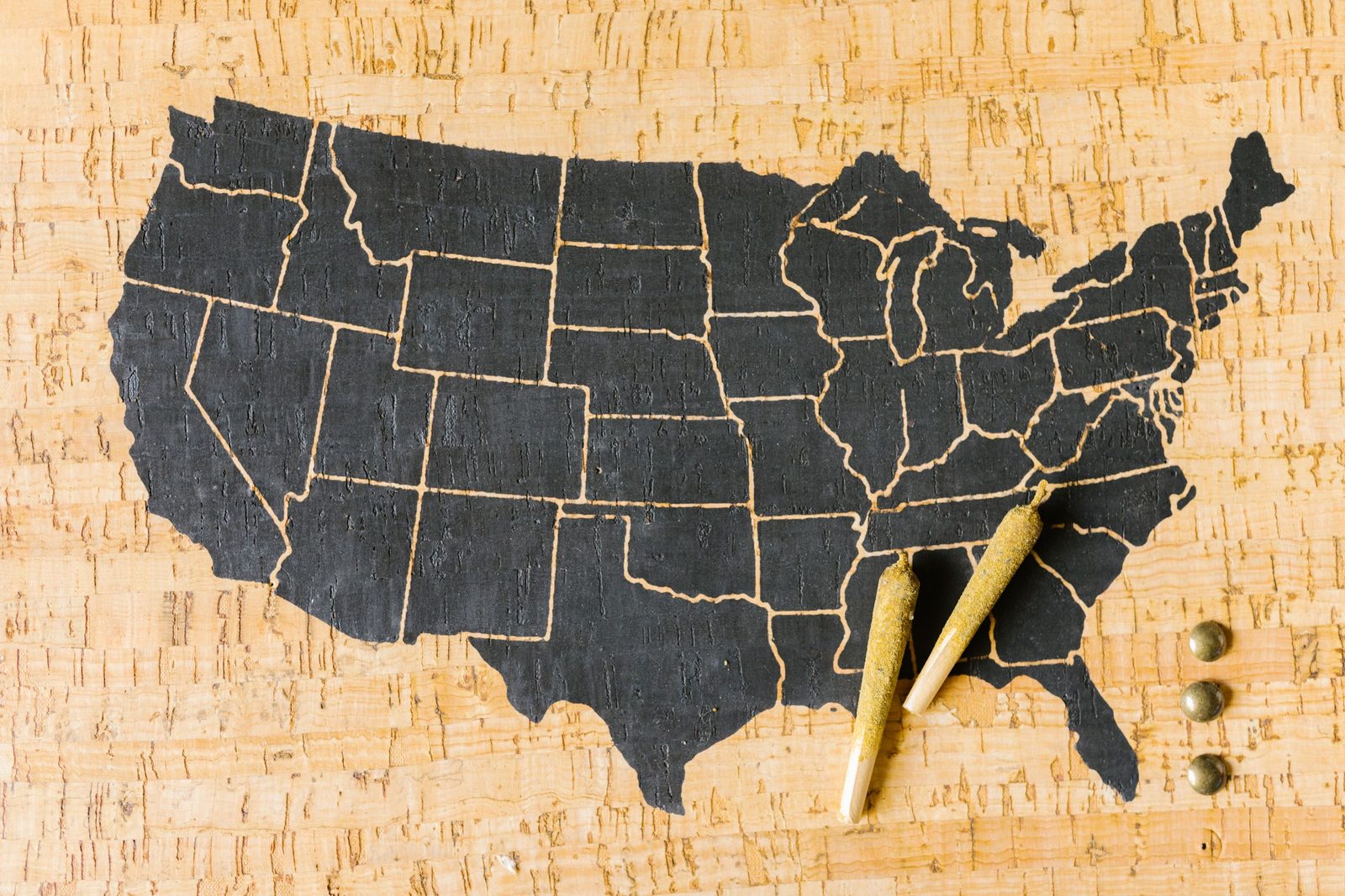 Map of the United States cut in dark board on cork, with two pins resting beside it