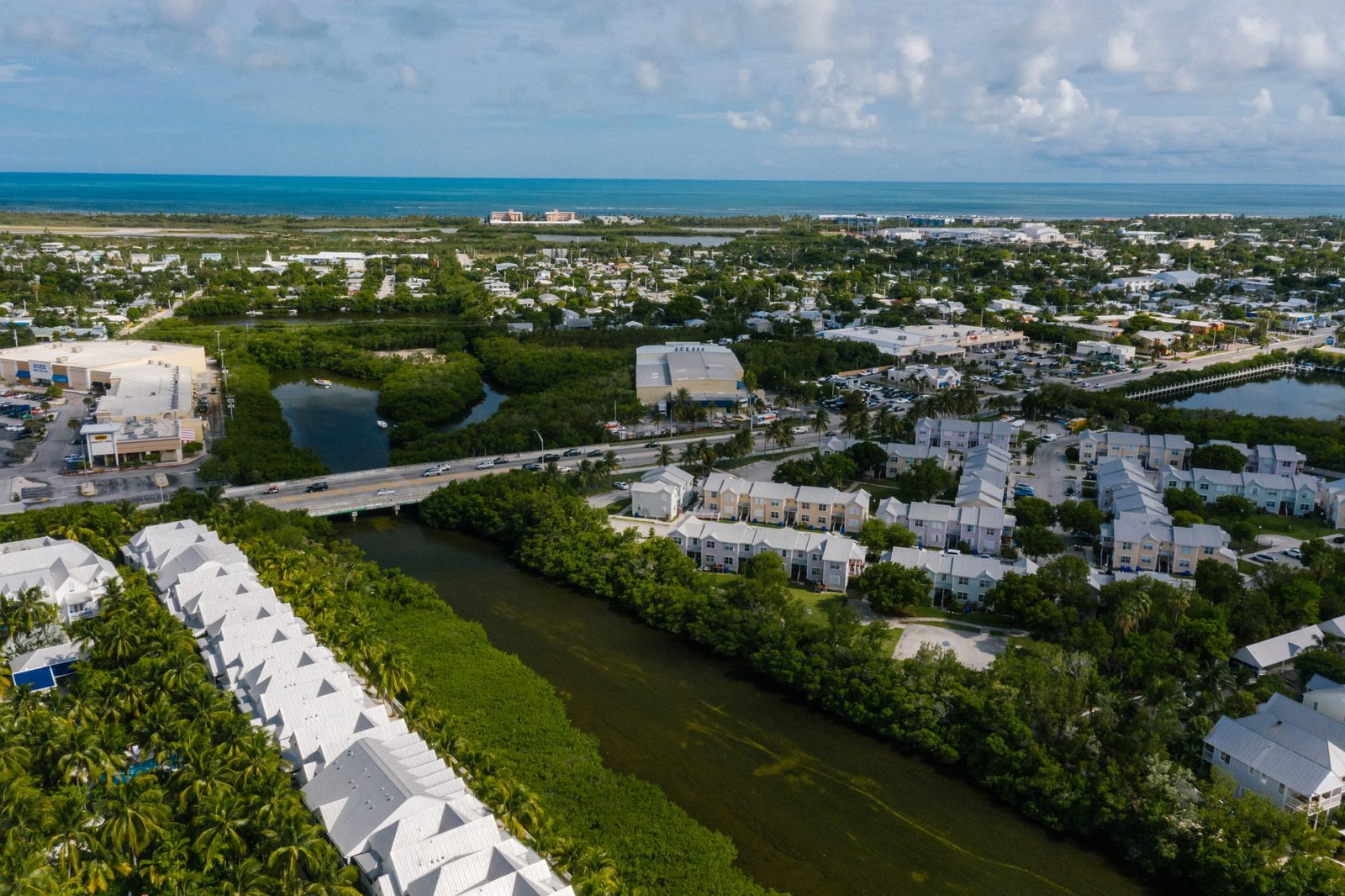 Aerial view of a coastal town beside a green waterway, ocean on the horizon