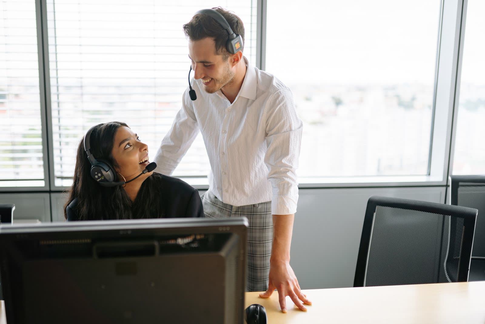 Supervisor helping an agent at a call-center desk by a window
