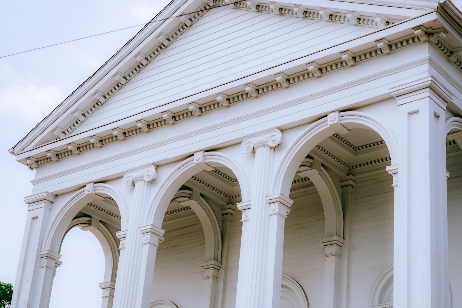 Arches and columns of a white neoclassical civic building against a bright sky