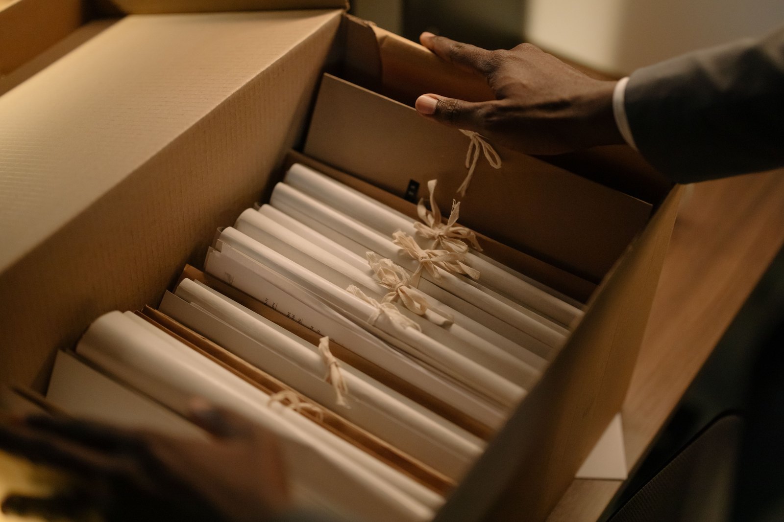 Hands lifting bundles of tied paper records out of an archive box