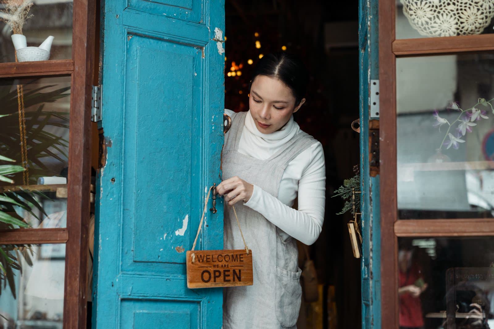 Shop owner turning the open sign on a blue storefront door