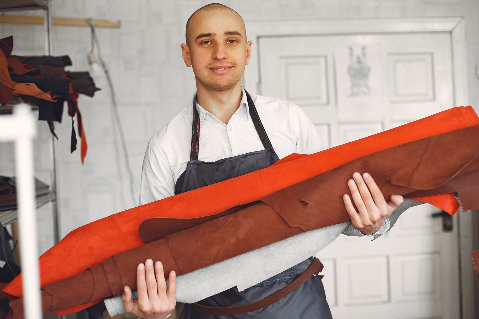 Leatherworker in an apron holding rolled hides in his workshop