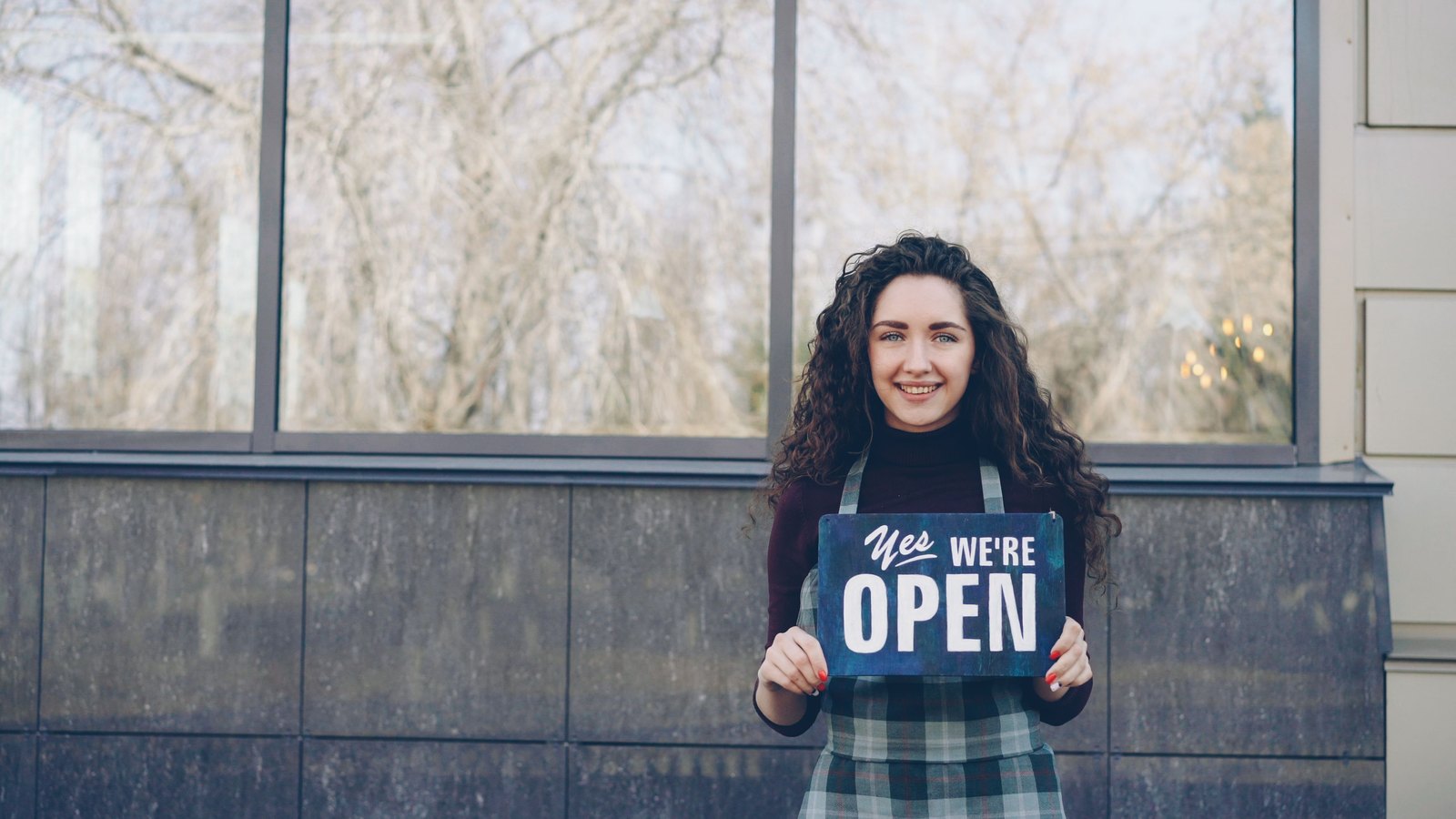 Shop owner holding an open sign in the window of a new business